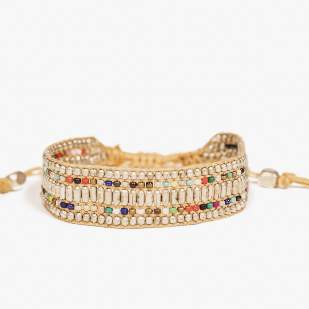 Photograph of a multi-strand beaded bracelet featuring rows of silver-colored round and tube beads interspersed with vibrant colorful seed beads on a light tan cord against a clean white background