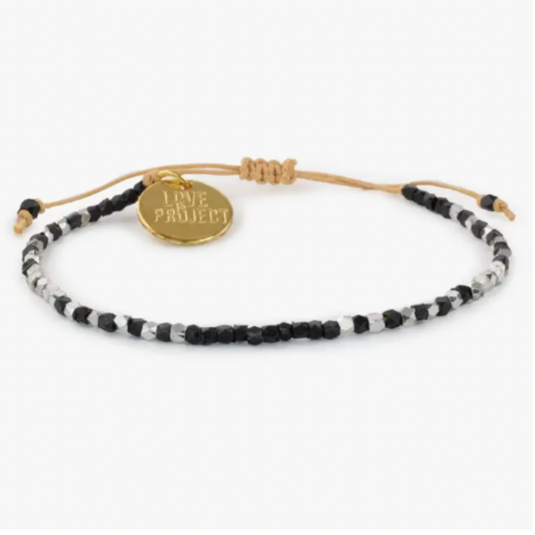 Beaded bracelet featuring black and silver faceted beads on an adjustable tan cord with a gold-tone 'LOVE PROJECT' charm