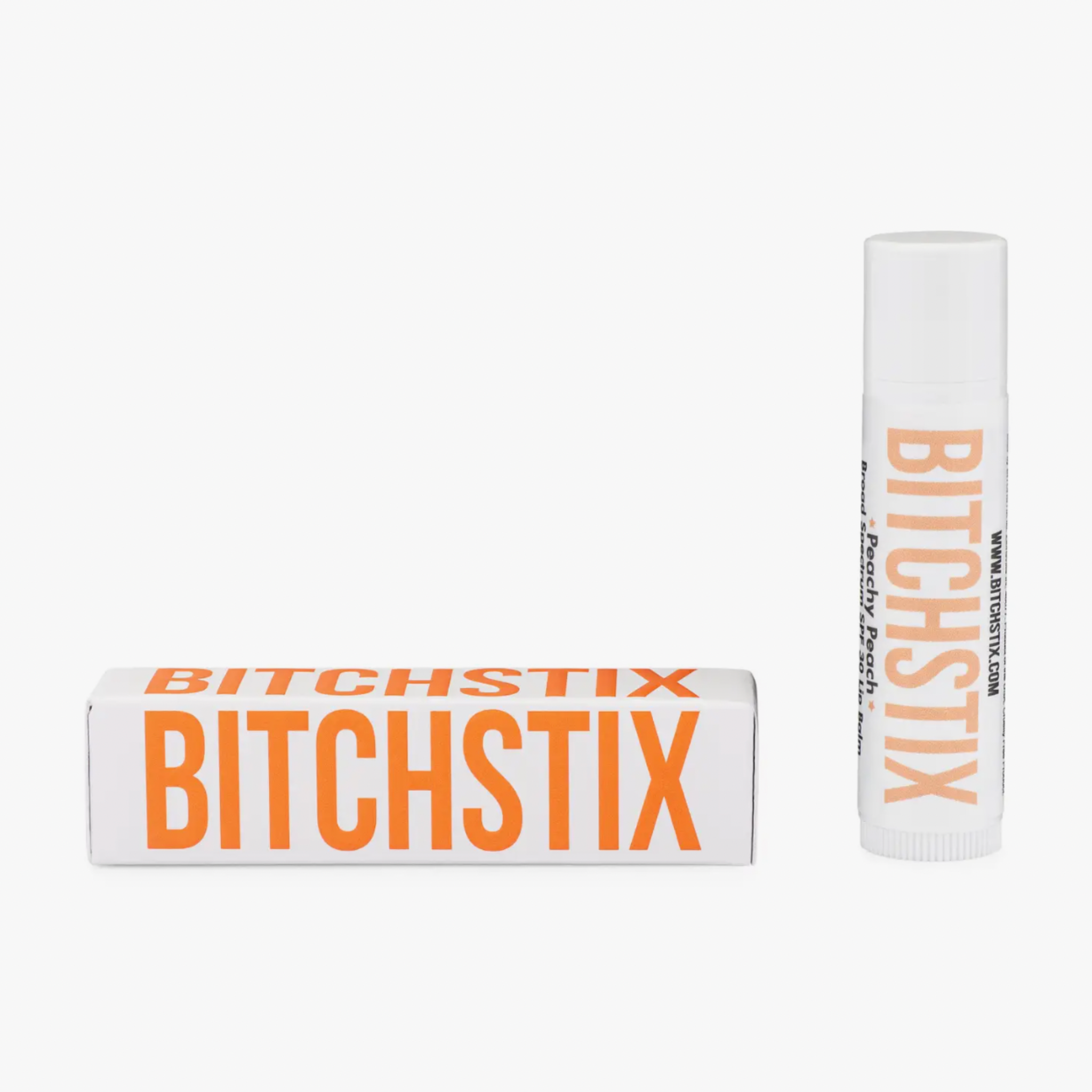 Product photography of a Bitchstix Peachy Peach Broad Spectrum SPF 30 lip balm white tube and its horizontal white box packaging with bold orange branding on a plain white background