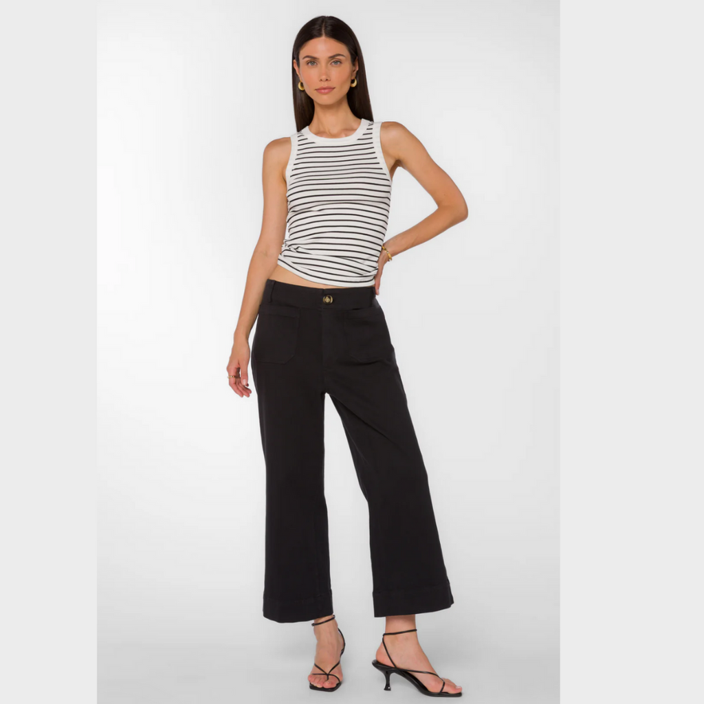 Photographic image of a woman modeling a white and black striped tank top, black wide-leg cropped trousers with a brown button, and strappy black kitten heel sandals on a white studio background