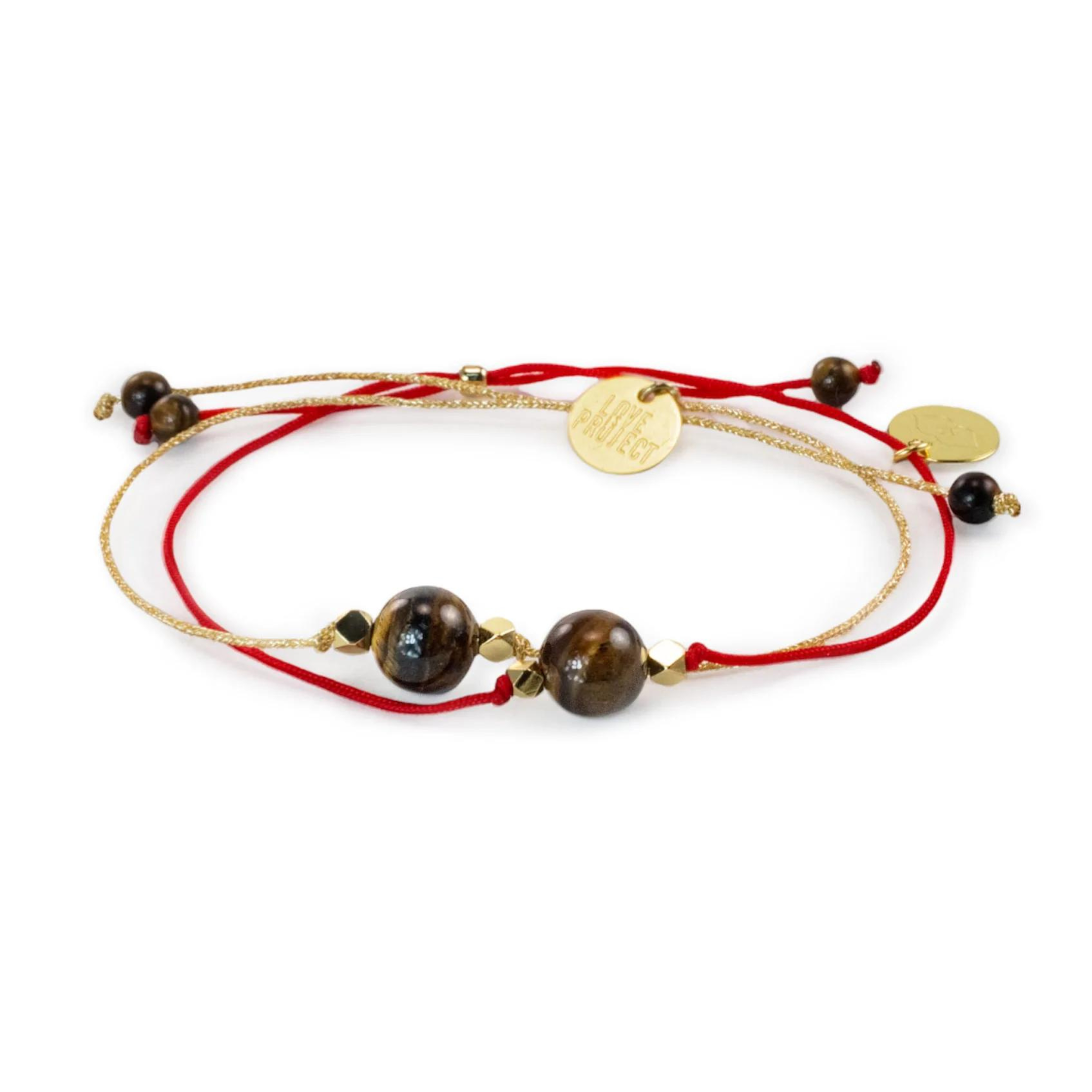 Jewelry bracelet with intertwined red and gold cords, two polished brown tiger eye beads, gold faceted spacers, and a round gold LOVE PROJECT charm on a white background