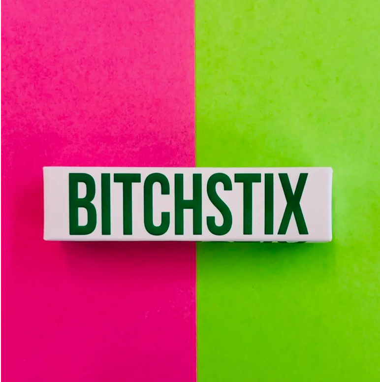 A white rectangular box with dark green BITCHSTIX text centered horizontally against a vibrant split background of neon pink and lime green